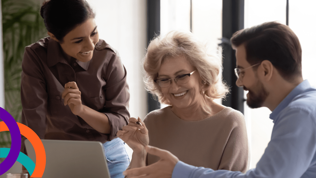 Team look at a document. Sat in the middle is a lady with long hair and glasses, to her left a younger woman and to her right a man wearing glasses. They are all smiling